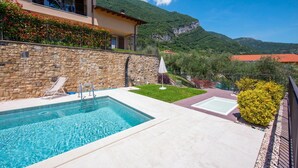 A swimming pool with a stone wall, a grassy area, and a mountain backdrop.