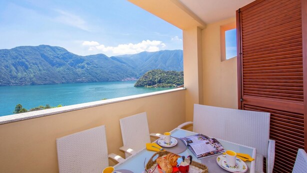A balcony with a table set for breakfast, overlooking a lake and mountains.