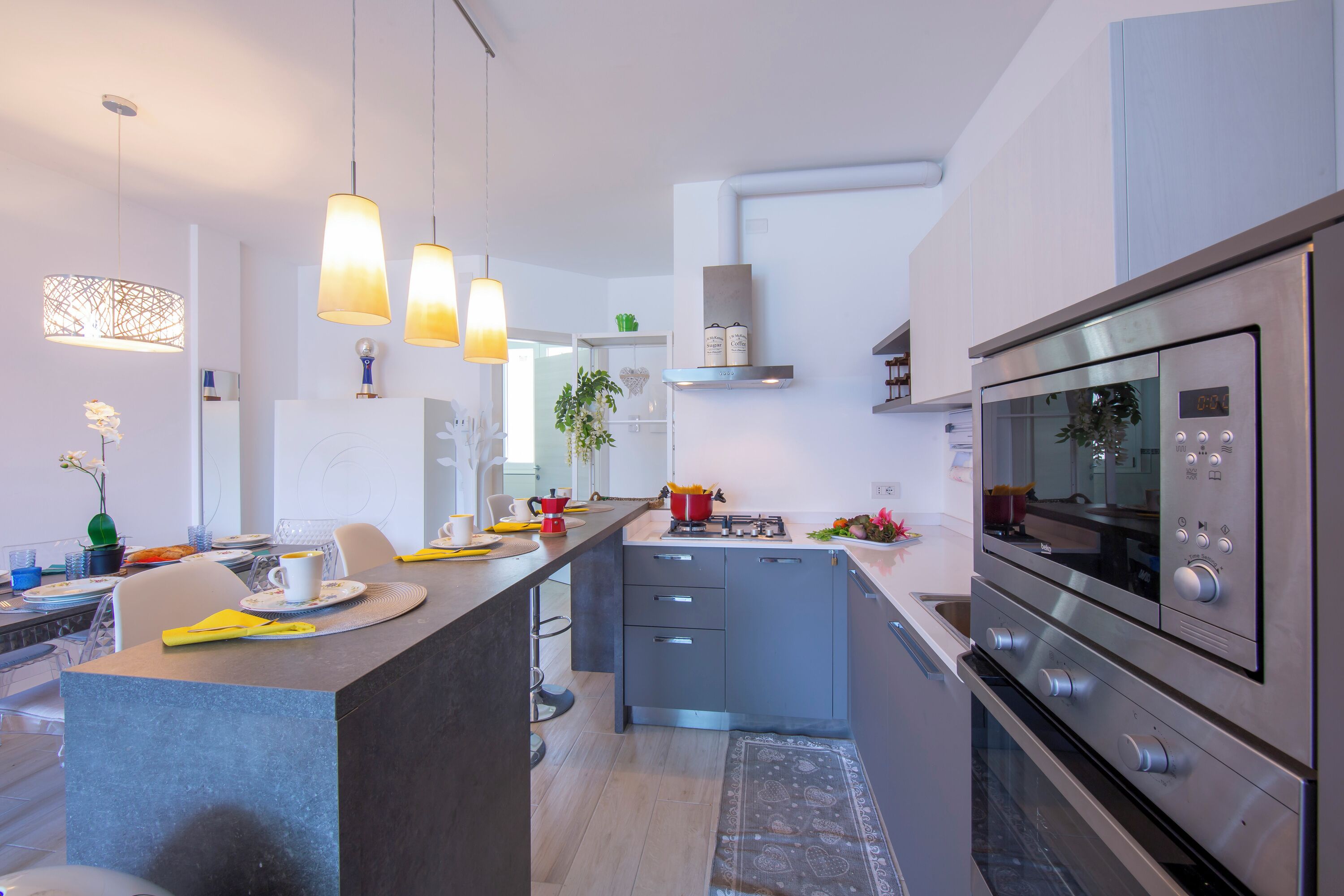 Une cuisine moderne dotée d’un îlot central, d’appareils électroménagers en acier inoxydable, de luminaires suspendus et d’une horloge bien visible.