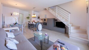 A modern living space with a sofa, glass coffee table, kitchen area, and a staircase.