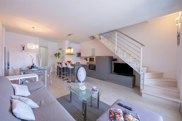 Ein zeitgemäßer Wohnbereich mit Sofa, Glastisch, Küchenzeile und Treppe.