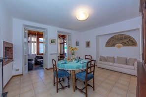 A dining area with a table, chairs, a vase with flowers, and a sofa in the background. - Casa Mira Al Lago (Menaggio)