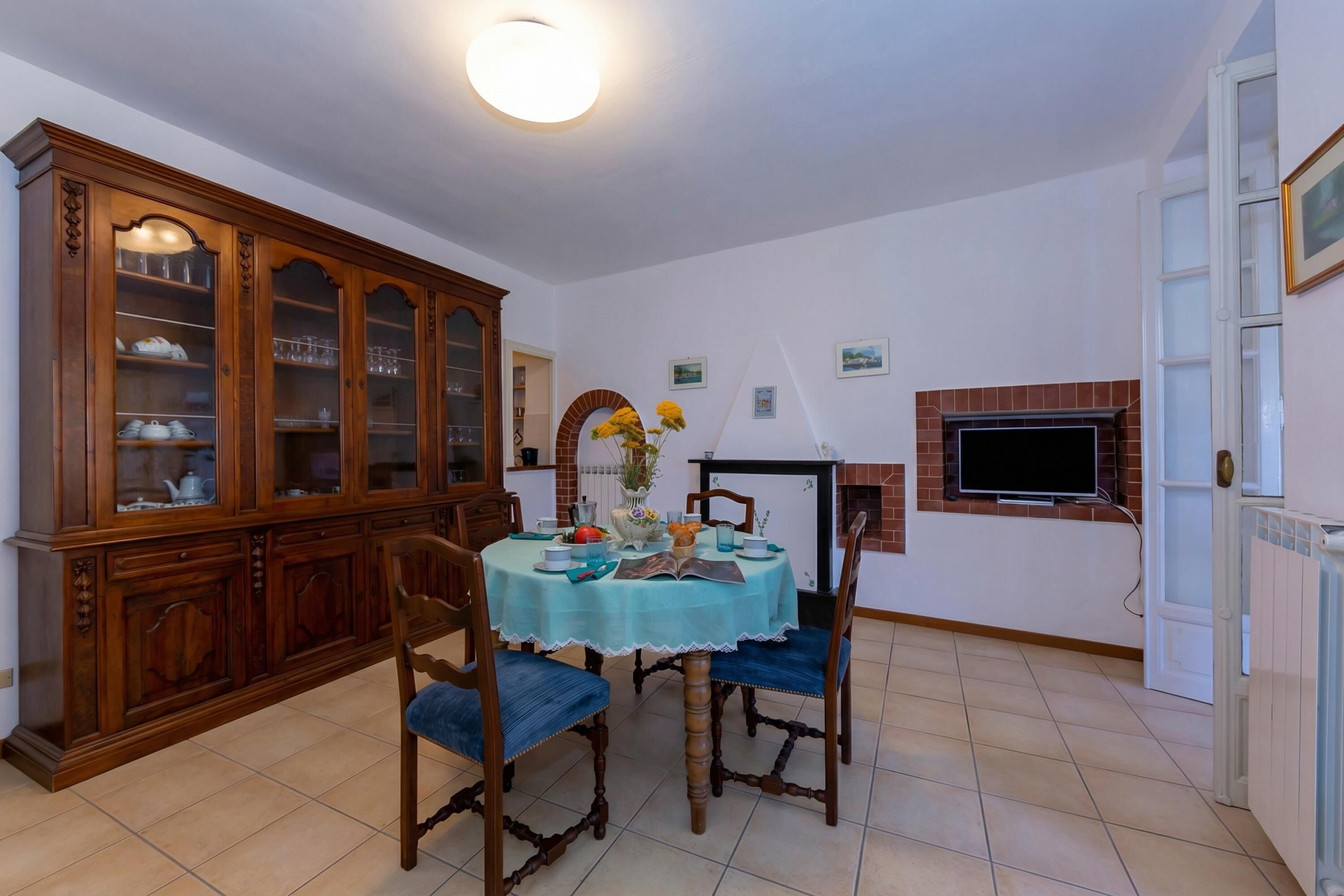 A dining area with a wooden cabinet, a round table with chairs, a fireplace, and a television mounted on the wall.