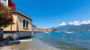 A waterfront building with arched windows, a stone wall, and boats in the water. - Casa Mira Al Lago (Menaggio)
