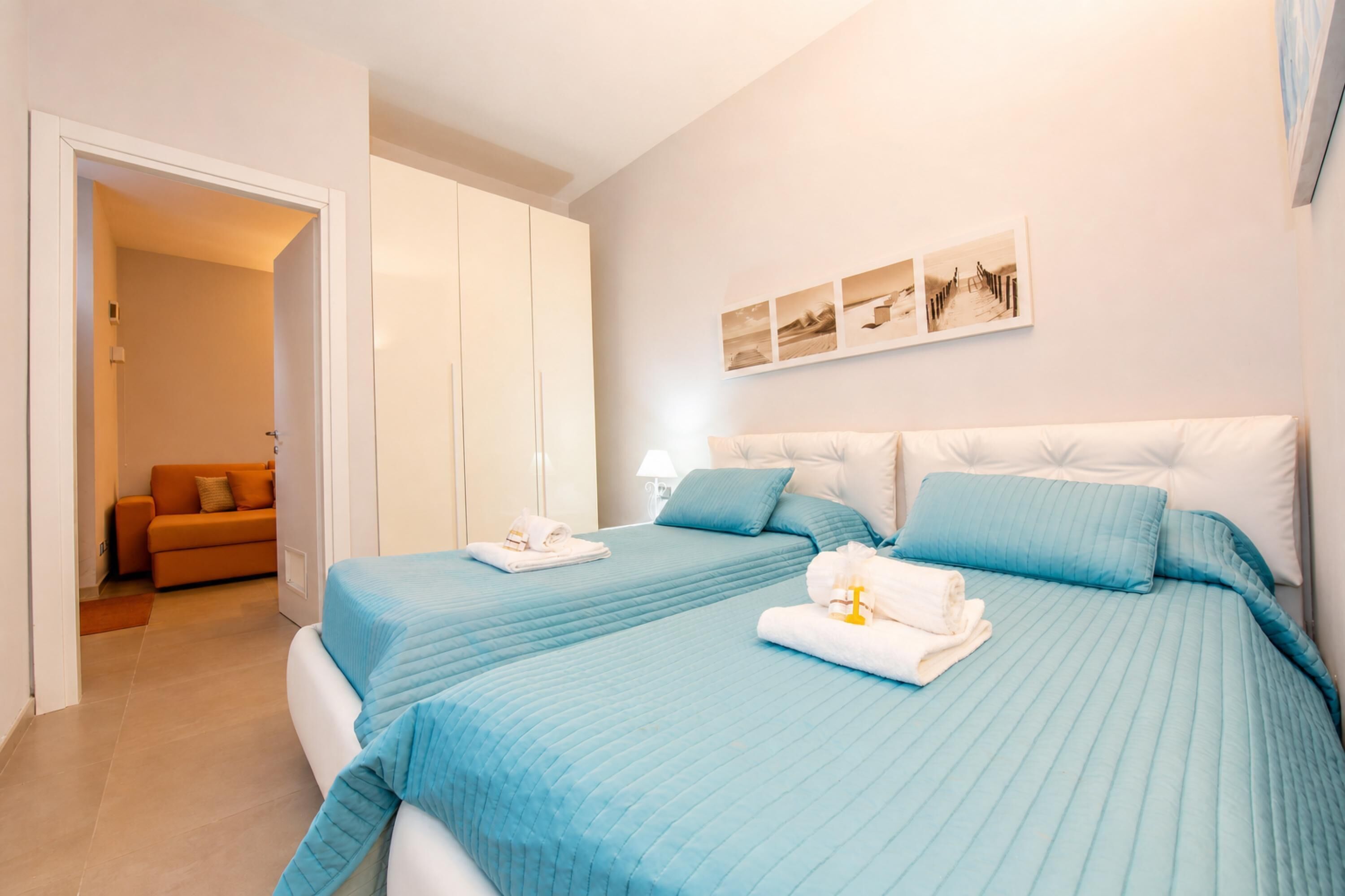 A hotel room with two beds, a wardrobe, a sofa, and a wall-mounted artwork.