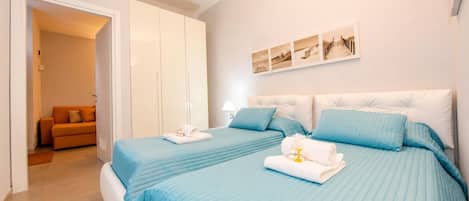 A hotel room with two beds, a wardrobe, a sofa, and a wall-mounted artwork.