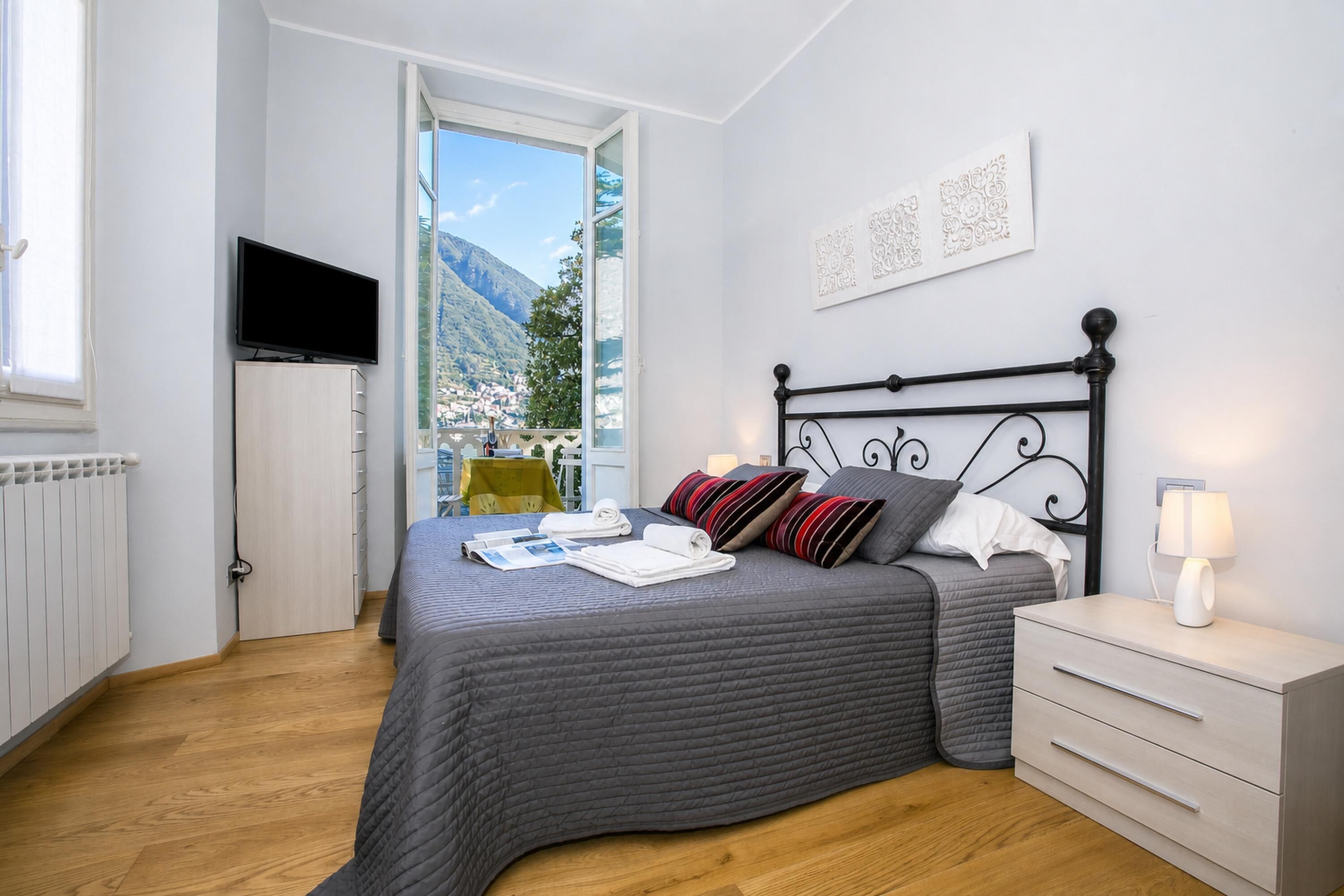 A bedroom with a bed, a TV, a bedside table with a lamp, and a view of a mountain.