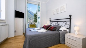 A bedroom with a bed, a TV, a bedside table with a lamp, and a view of a mountain. - Villa Lucia Laglio (Laglio)