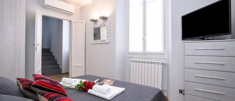 A hotel room with a bed, a TV, a mirror, and a window.