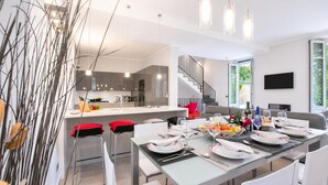 A modern kitchen with a dining area set for a meal, a staircase, and a TV mounted on the wall. - Villa Lucia Laglio (Laglio)