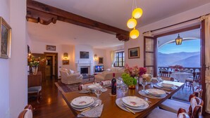 Un comedor con una mesa de madera dispuesta para seis comensales, una chimenea y vistas a montañas a través de un amplio ventanal.