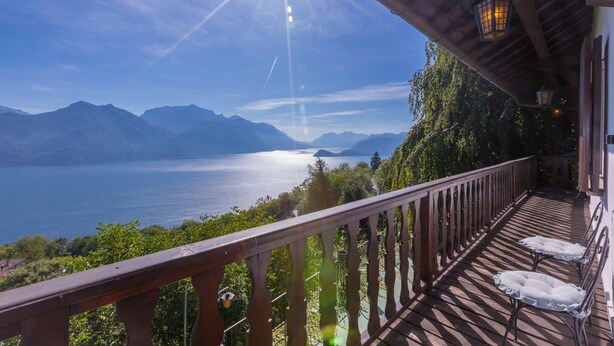 Una terraza de madera con barandilla que da a un lago y montañas.