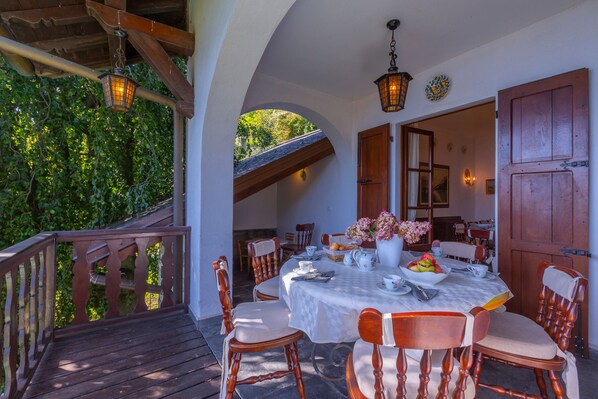 An outdoor dining area with a wooden deck, white tablecloth-covered table, and wooden chairs. - Villa La Volpe Plesio (Plesio)