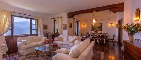 A spacious living room with a large window, a dining area, and a wooden ceiling.