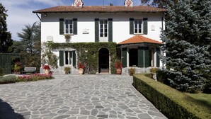 A two-story building with a tiled roof, green shutters, and a stone-paved entrance. - Villa Silvana (Oliveto Lario)