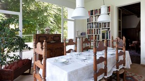 A dining area with a table set for six, surrounded by wooden chairs with intricate carvings. A large bookshelf filled with books is visible in the background. - Villa Silvana (Oliveto Lario)