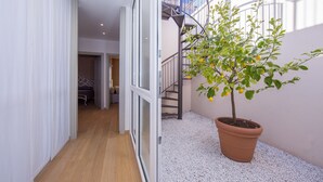 A narrow hallway with a potted lemon tree, a staircase, and a glimpse of a room with a bed.