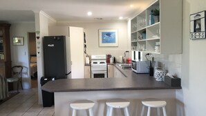 Eine moderne Küche mit Kochinsel, weißen Barhocker und einem Essbereich mit Blick auf das Wohnzimmer.