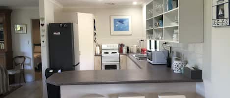 Uma cozinha moderna com ilha central, banquetas brancas e uma área de jantar com vista para a sala de estar.