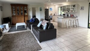 Ein modernes Wohnzimmer mit einer schwarzen Couch, einem Couchtisch und einem Bücherregal. Es gibt eine Küchenzeile mit einer Bar und Hockern.