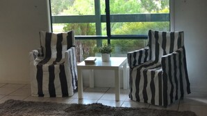 Ein Zimmer mit zwei gestreiften Sesseln, einem kleinen Tisch mit einer Pflanze und Blick auf Grün durch ein großes Fenster.