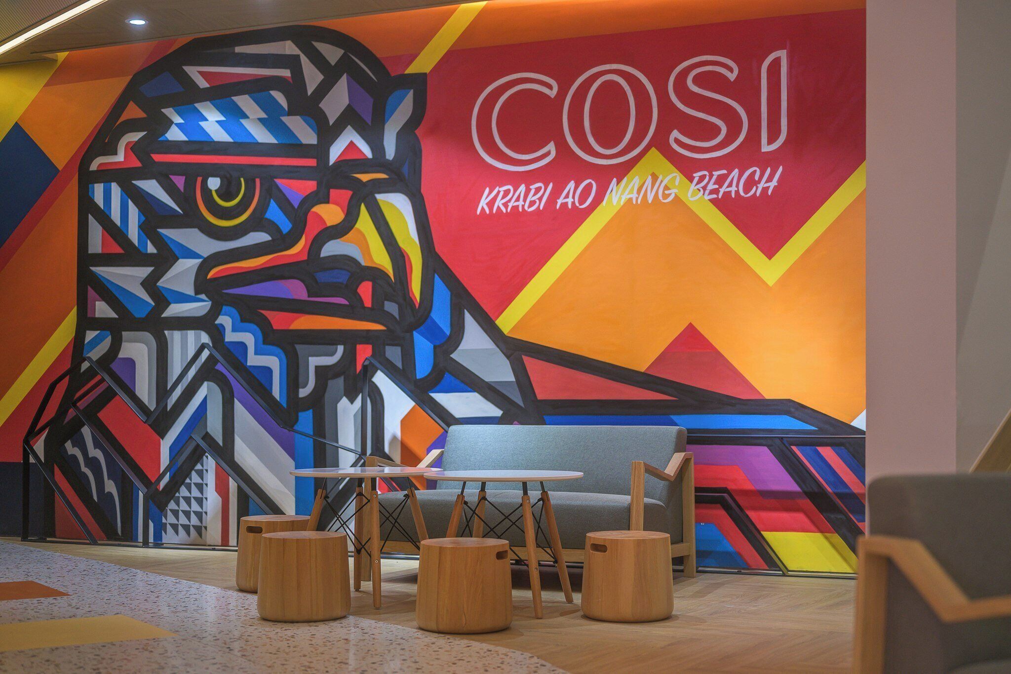 Un interior moderno con un mural colorido, un sofá y taburetes de madera.