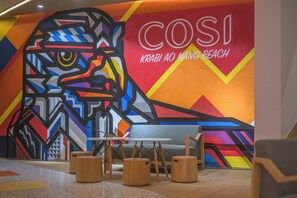 Un interior moderno con un mural colorido, un sofá y taburetes de madera.