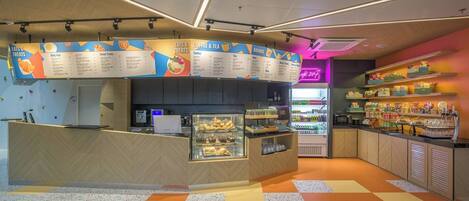 A café with a menu board, a coffee machine, and a display of drinks.