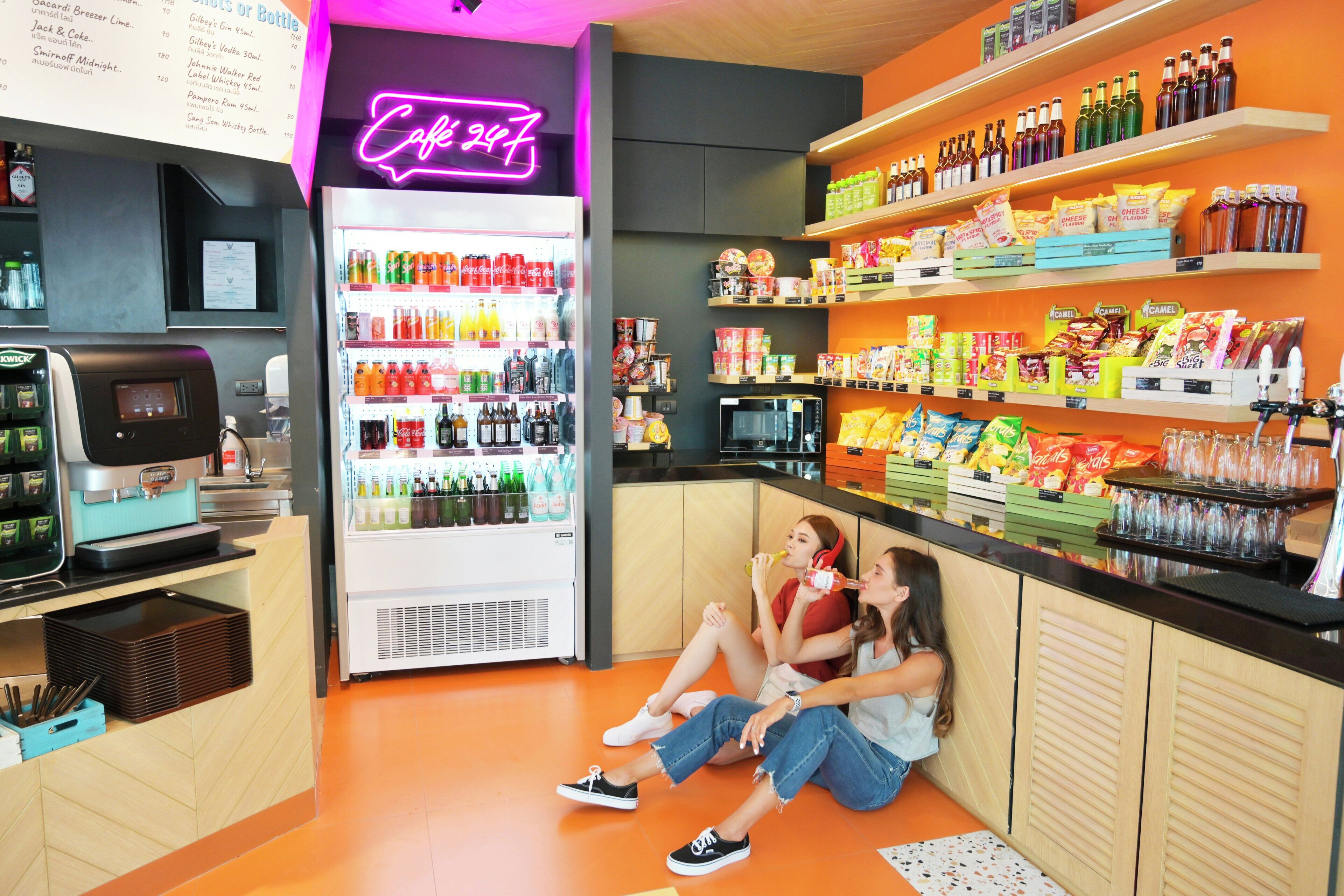 Un bar de aperitivos bien iluminado con un letrero de neón, un dispensador de bebidas y estantes llenos de comida y refrescos.