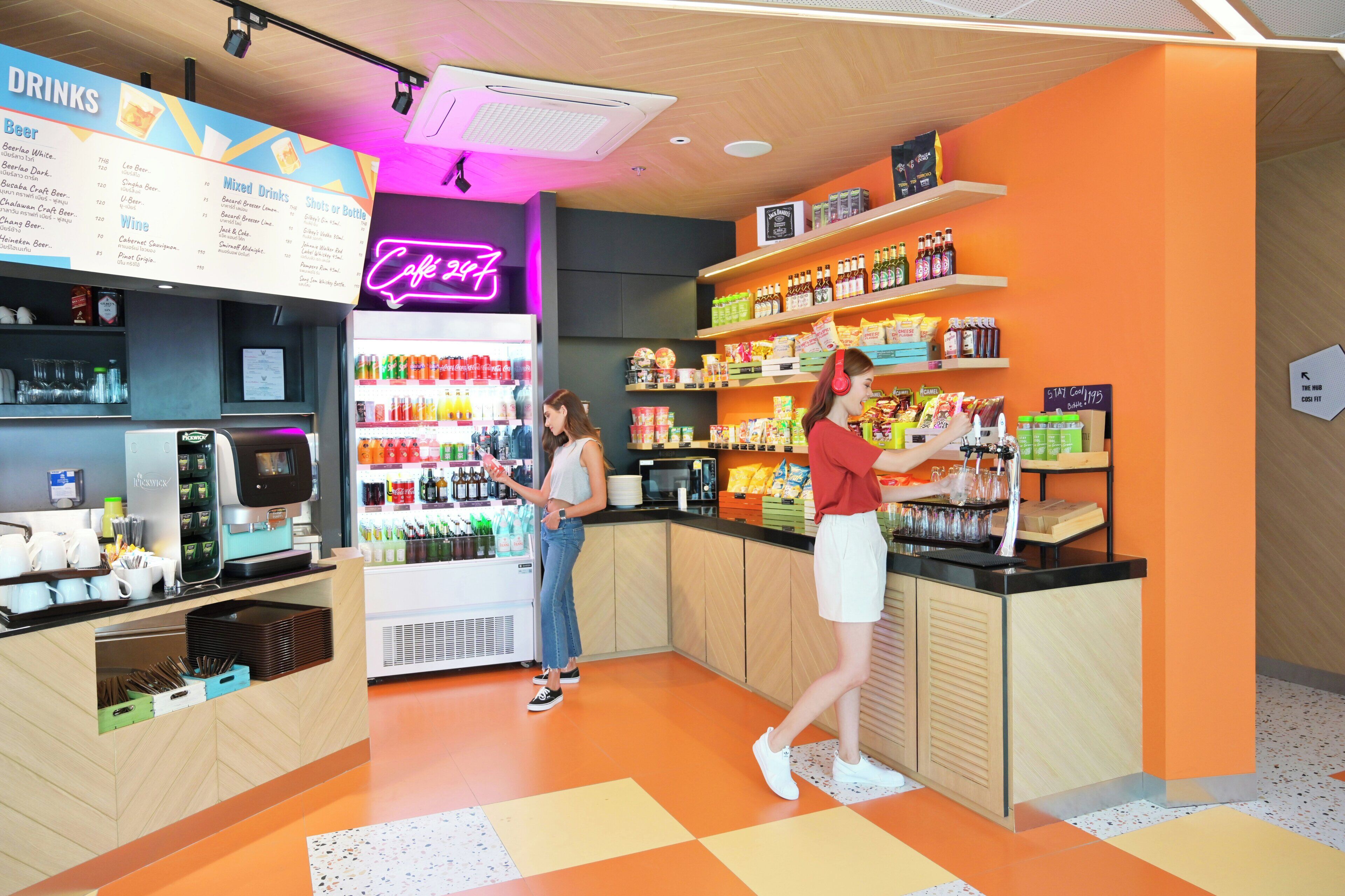 Una cafetería con una pizarra de menú, un letrero de neón, un dispensador de bebidas y estantes llenos de aperitivos y bebidas.
