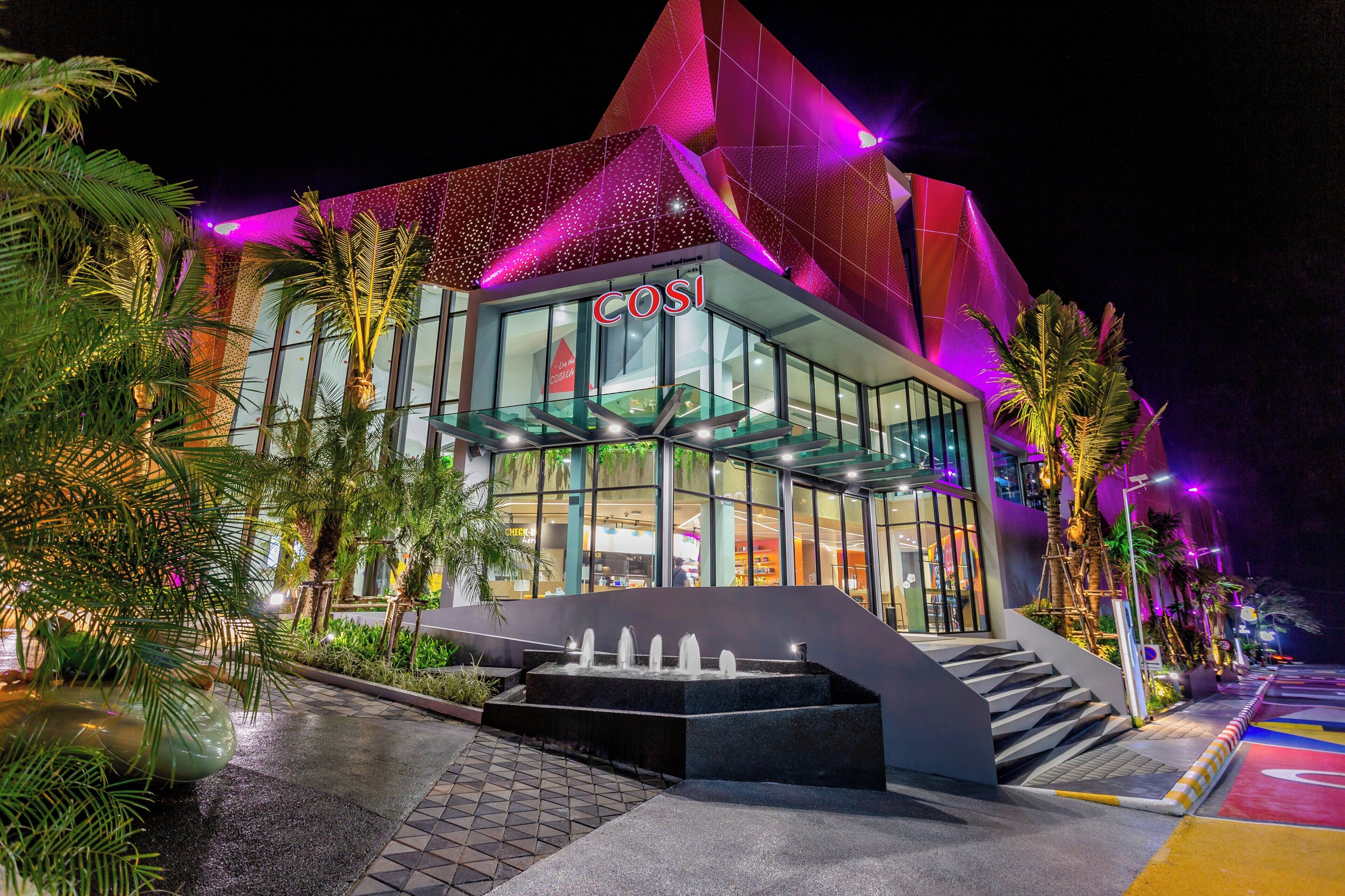 Un edificio moderno con fachada de vidrio, un llamativo letrero 'COSI' y un diseño de techo geométrico único.