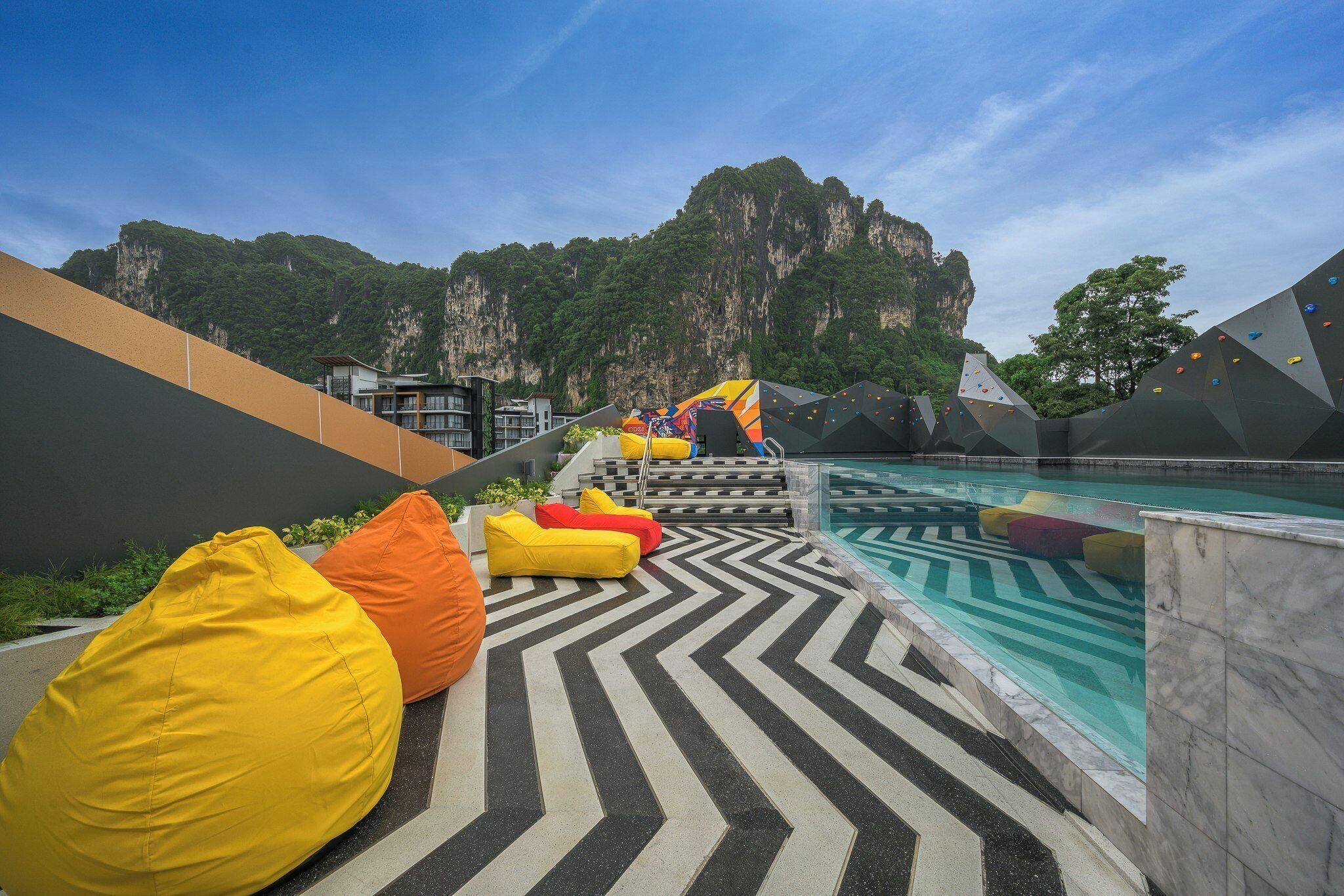 A pool area with colorful bean bags, a climbing wall, and a view of a mountainous landscape.