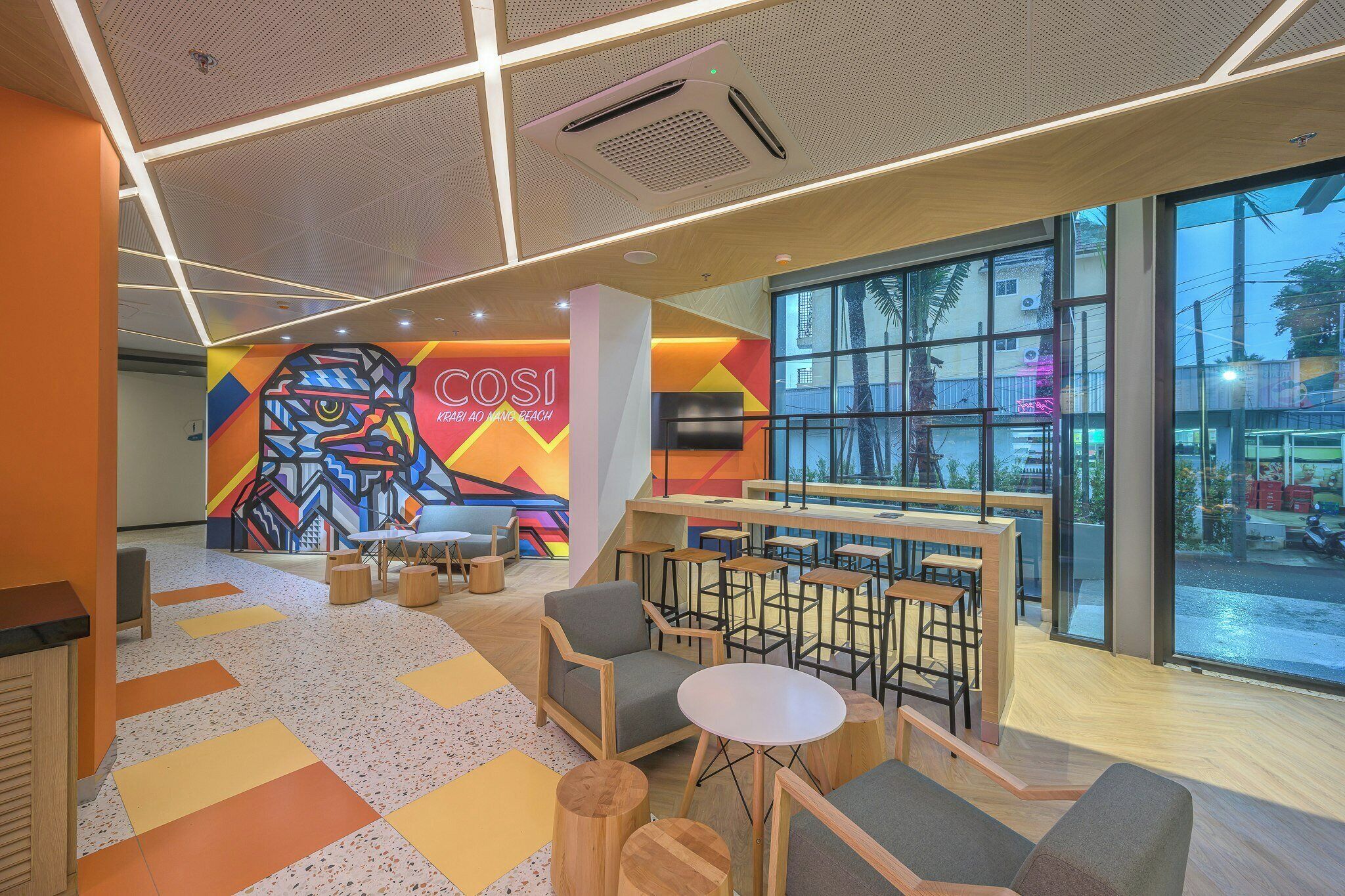 A modern interior with a colorful mural, seating area, and large windows.