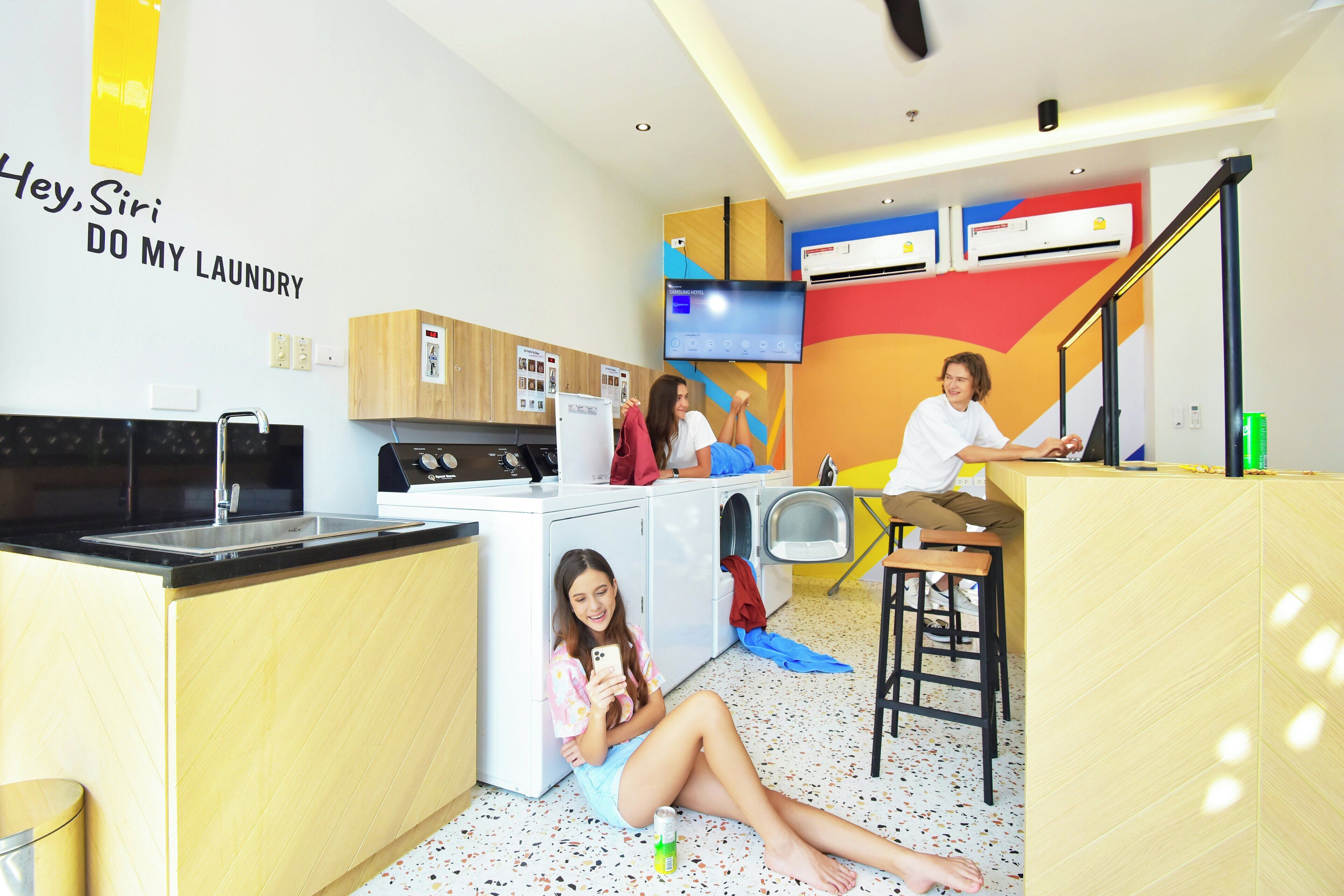 A compact hotel room with a kitchenette, a washing machine, a Samsung TV, and a bar area.