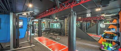 Un gimnasio con equipamiento de levantamiento de pesas, un saco de boxeo y una decoración en tonos rojo y negro.