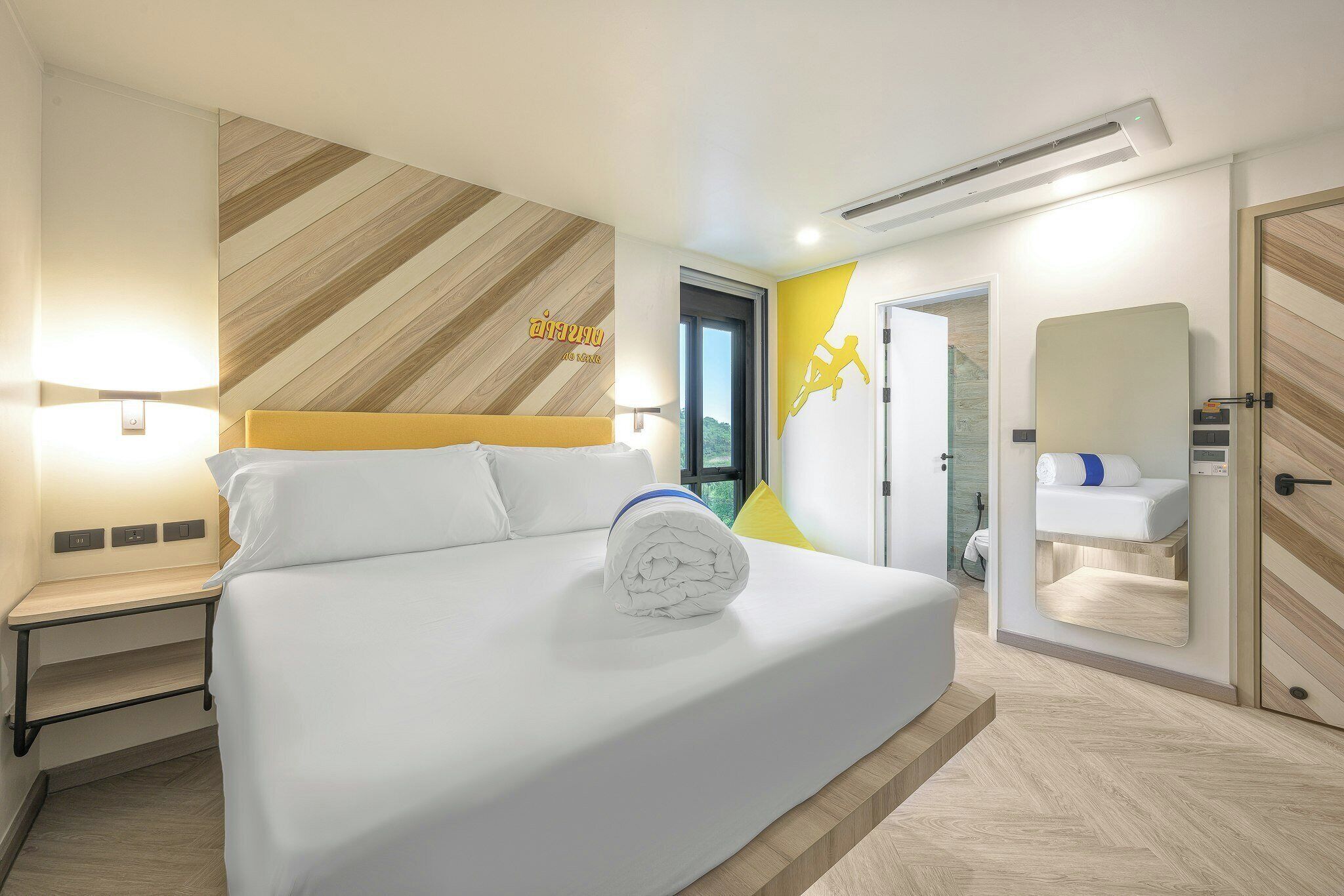 A hotel room with a bed, a bedside table, a mirror, and a bathroom with a shower.