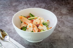 Eine weiße Schüssel mit Salat, bestehend aus Blattsalat, Hähnchen und Speck, auf einer strukturierten grauen Oberfläche.