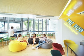 A modern interior with large windows, a yellow wall with 'THE HUB' signage, and seating areas with bean bags and chairs. - COSI Krabi Ao Nang Beach (Krabi)