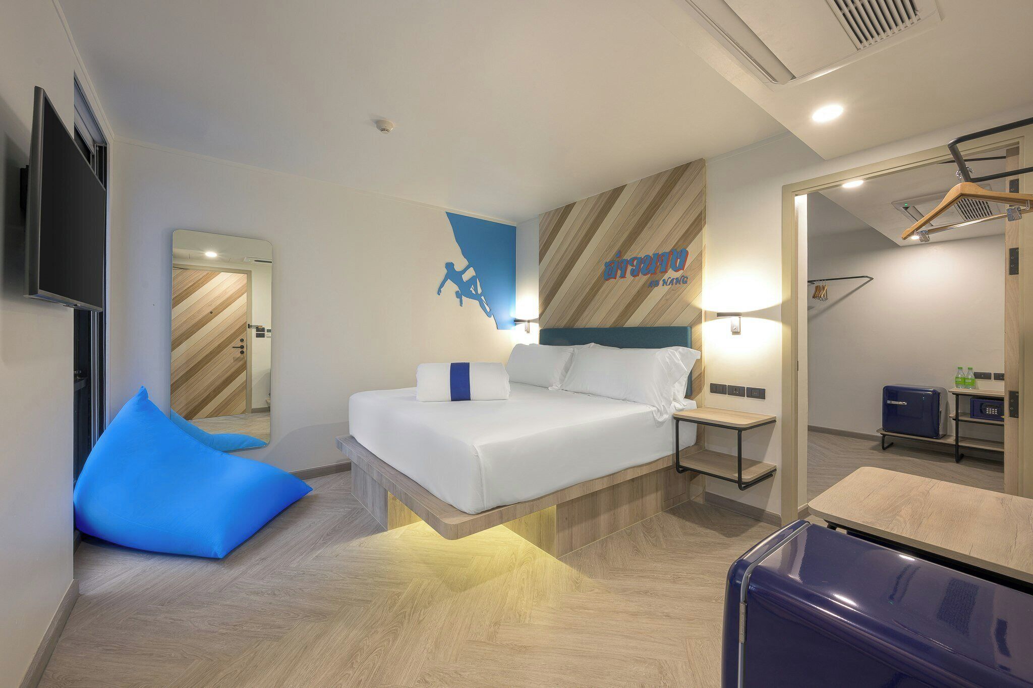 Ein modernes Hotelzimmer mit einem Bett, einem blauen Sitzsack, einem Nachttisch, einem Spiegel und einem Kleiderschrank.