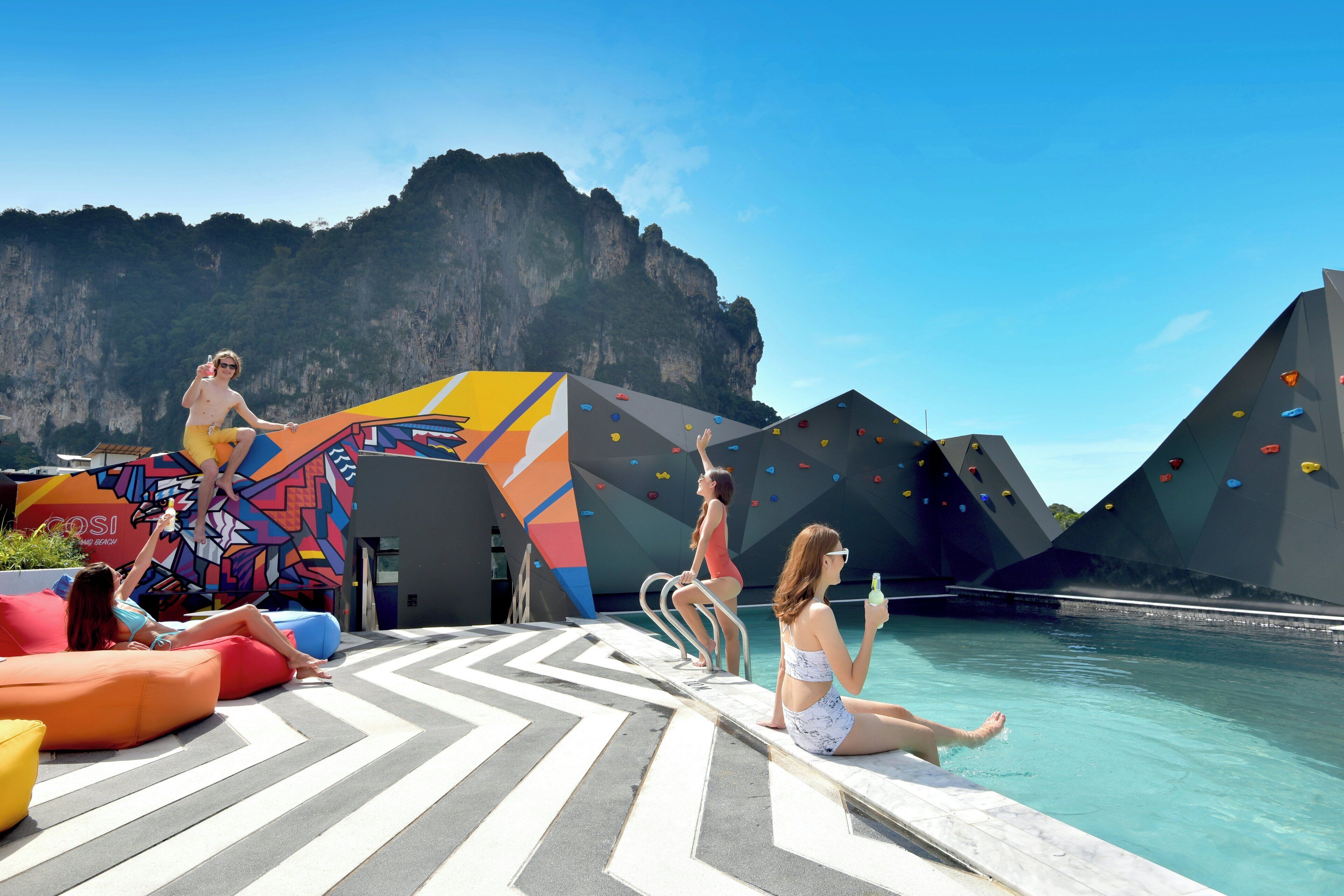 A poolside area with climbing walls, a colorful mural, and a clear view of a mountainous landscape.