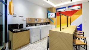 A modern laundry room with a sink, multiple washing machines, and a television mounted on the wall. - COSI Krabi Ao Nang Beach (Krabi)