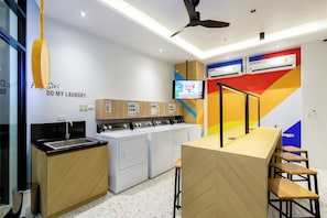 A modern laundry room with a sink, multiple washing machines, and a television mounted on the wall. - COSI Krabi Ao Nang Beach (Krabi)