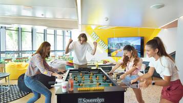 Un grupo de personas jugando al fútbol de mesa en un espacio interior luminoso con ventanas grandes y una pared amarilla.