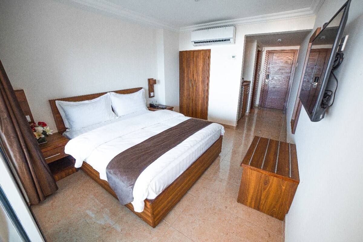 A hotel room with a wooden bed, a nightstand, an air conditioning unit, and a wardrobe.