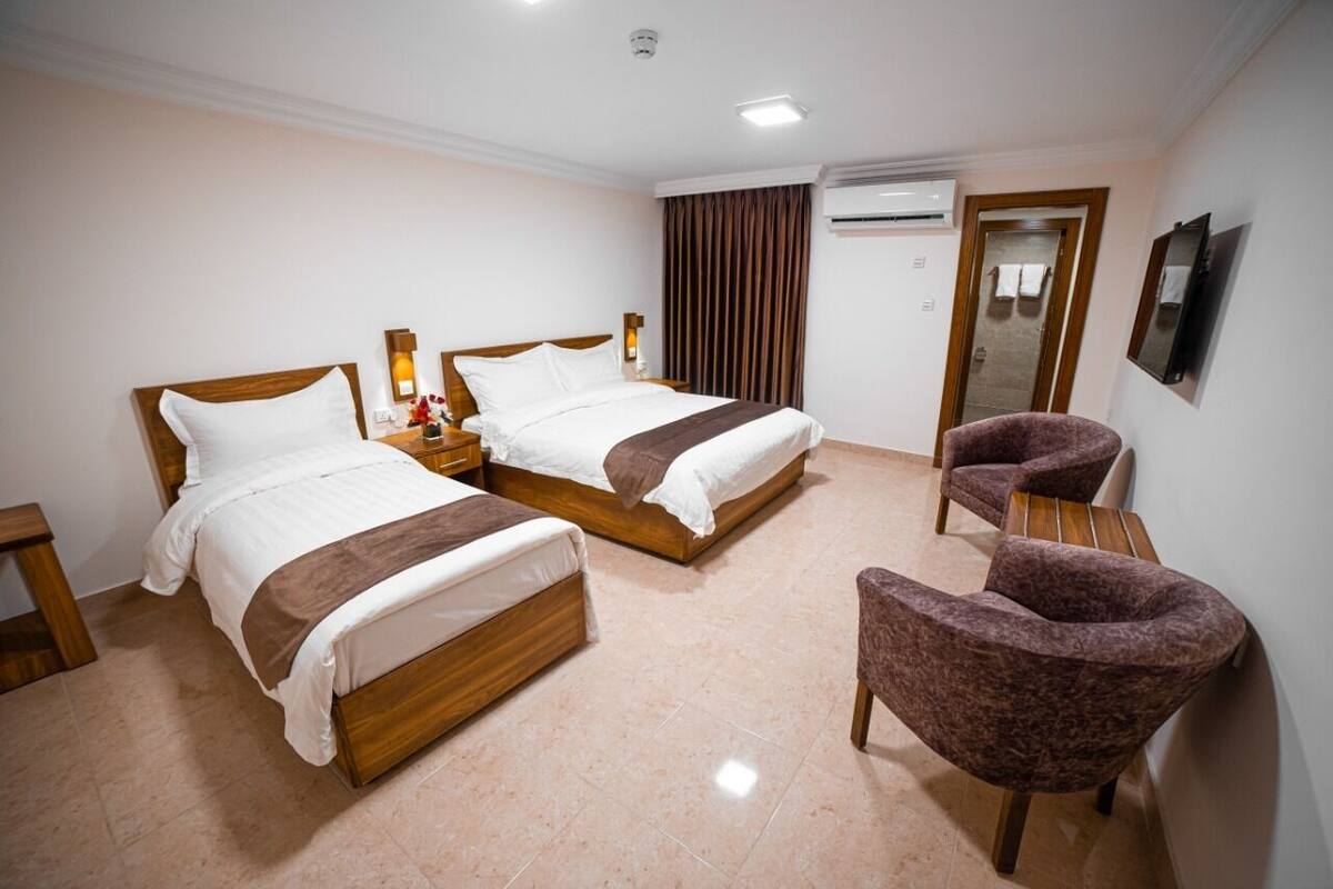 A hotel room with two wooden beds, a brown armchair, a small table, and a mirror on the wall.