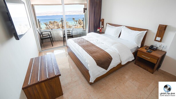 A hotel room with a bed, bedside table, and a view of the sea. - Joar Beach Hotel (Aqaba)