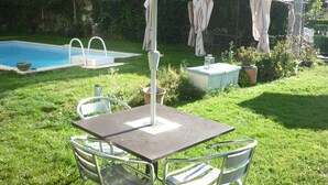 Een terras met een tafel en stoelen, een zwembad en een overdekt gebied met gordijnen.