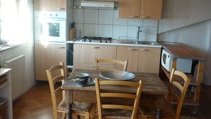 Een functionele keuken met houten kastjes, een gasfornuis en een eettafel met stoelen.