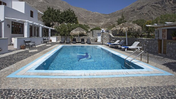 A swimming pool with lounge chairs and a mountain backdrop. - 3 Bedrooms Apartment included Car Rental (heated pool) (santorini)