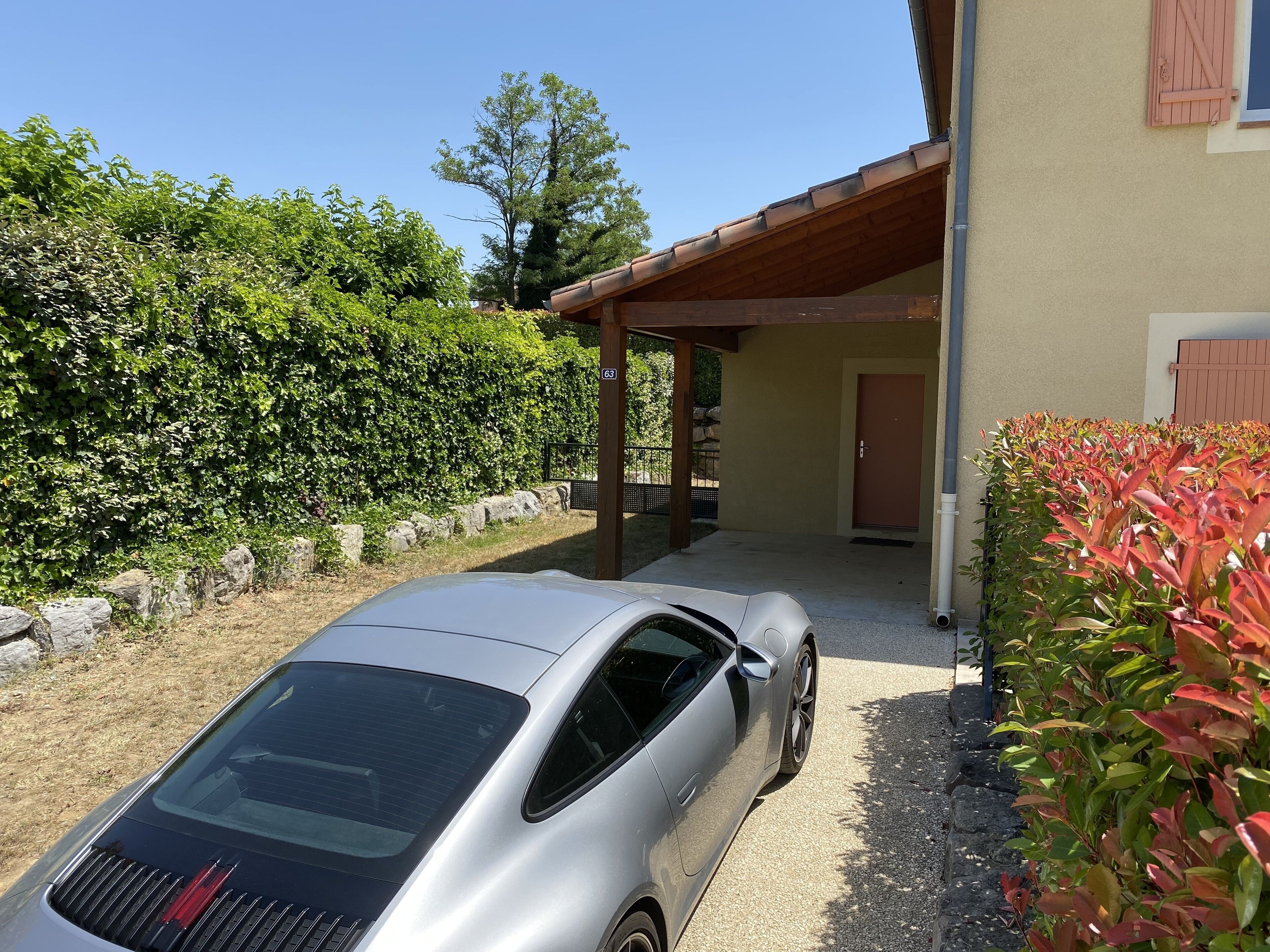 A silver car parked in front of a building with a covered porch and a door marked with the number 63.